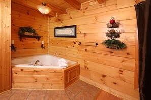 A wooden cabin bathroom with a bathtub, a framed certificate, and wall-mounted hooks with greenery. - Amazing Grace - Two Bedroom Cabin (Sevierville)