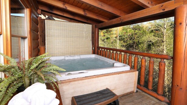 A wooden deck with a hot tub, a wooden bench, and a potted plant. - Amazing Grace - Two Bedroom Cabin (Sevierville)