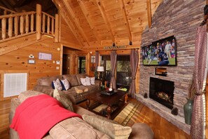 A cozy log cabin interior with a wooden staircase, a fireplace, a television, and a couch with a red blanket. - Amazing Grace - Two Bedroom Cabin (Sevierville)