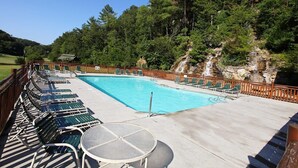 A swimming pool with lounge chairs and a table, surrounded by a wooden fence and trees. - Amazing Grace - Two Bedroom Cabin (Sevierville)