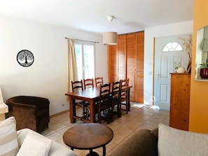 A dining area with a wooden table and chairs, a sofa, a small round table, and a wall-mounted tree decal.
