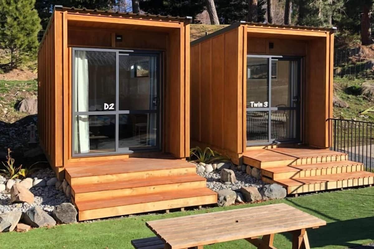 Two wooden cabins with glass doors, labeled 'D2' and 'Twin 3,' and a picnic table in front.