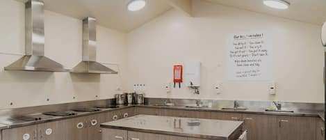 A kitchen with stainless steel appliances, wooden cabinets, and a sign with kitchen rules.