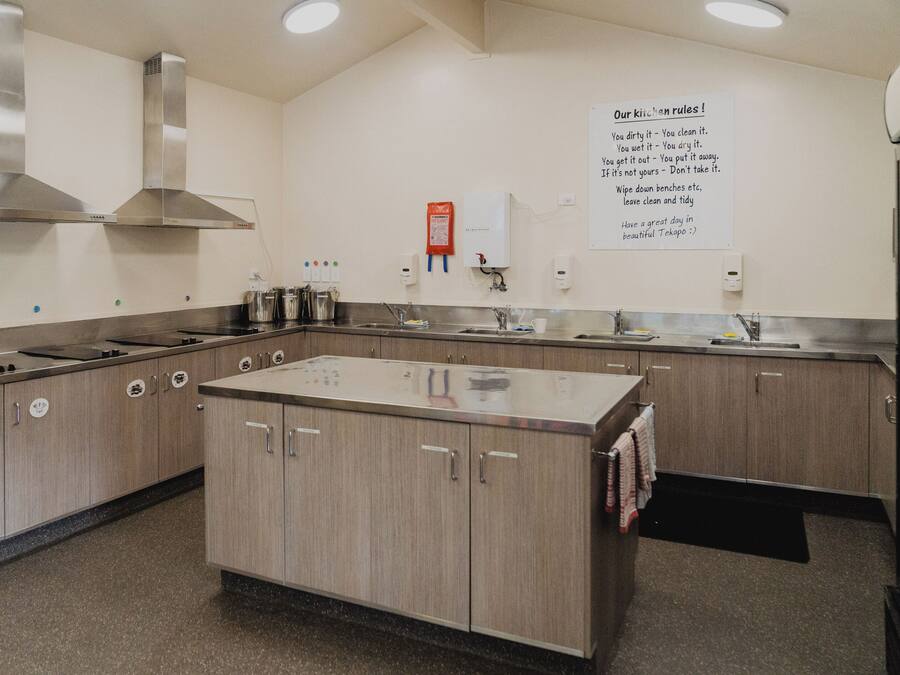 Uma cozinha com eletrodomésticos de aço inoxidável, armários de madeira e um aviso com as regras da cozinha.