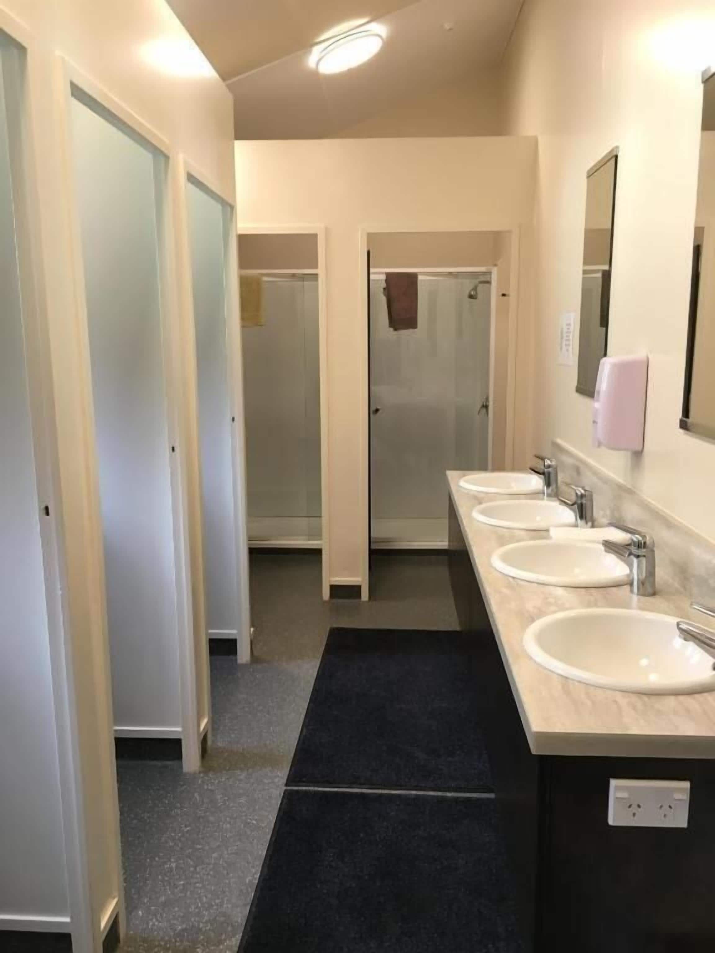 Ein Hotelbad mit drei Waschbecken, einer Dusche und einem Spiegel.