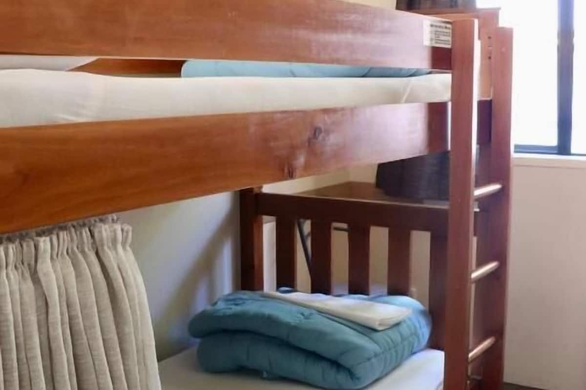 A bunk bed with a wooden frame, a lower bunk with a mattress and pillows, and a window with curtains.