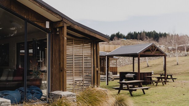 A building with a glass door, wooden shutters, and a covered outdoor seating area with picnic tables. - Lakes Edge Lodge (Lake Tekapo)