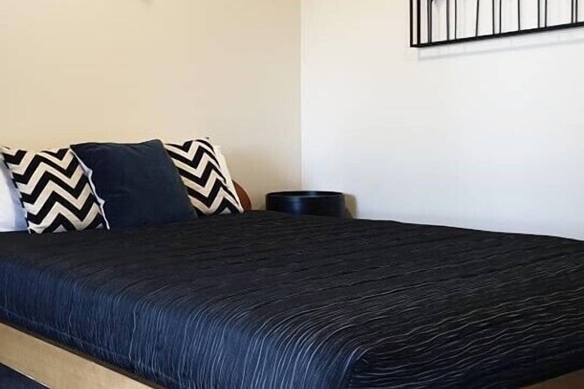 A bed with a dark blue bedspread, two black nightstands, and a wooden headboard.