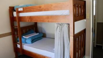 A bunk bed with a wooden frame, a lower bunk with a grey mattress and a white sheet, and a top bunk with a blue mattress and pillows.