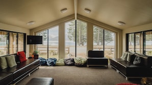 A modern interior with a large window, a sofa, a television, and a plant. - Lakes Edge Lodge (Lake Tekapo)