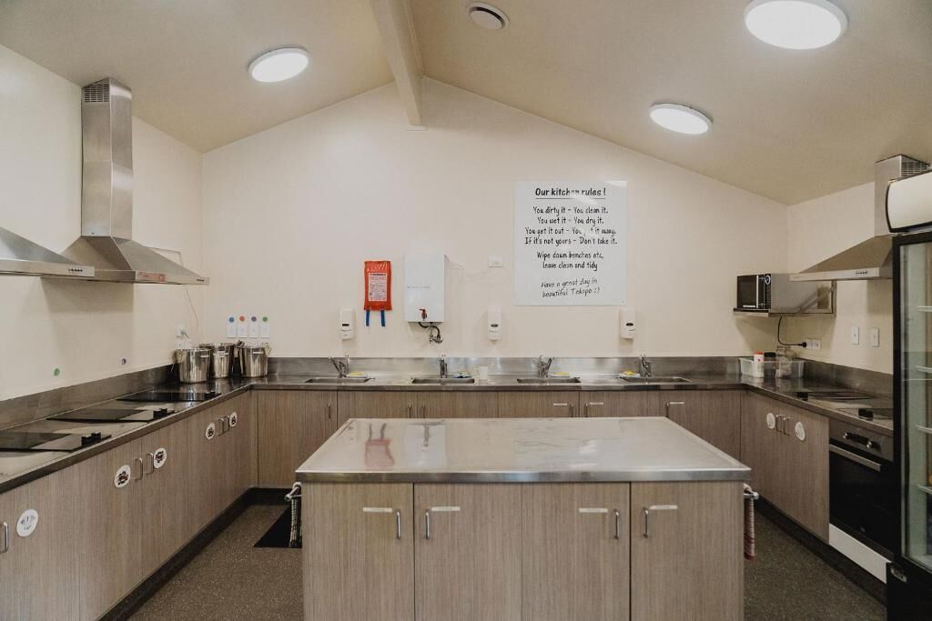A modern kitchen with stainless steel appliances, a central island, and a wall-mounted sign with kitchen rules.