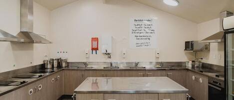 A modern kitchen with stainless steel appliances, a central island, and a wall-mounted sign with kitchen rules.