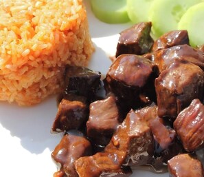 A plate with orange rice and dark brown cubes, possibly meat, with green vegetables on the side. - Sovanphum Riverside Hotel (Phnom Penh)