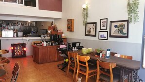 A dining area with wooden chairs, a table, a small dog, and a bar area with various items. - Sovanphum Riverside Hotel (Phnom Penh)