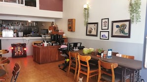 A dining area with wooden chairs, a table, a small dog, and a bar area with various items. - Sovanphum Riverside Hotel (Phnom Penh)