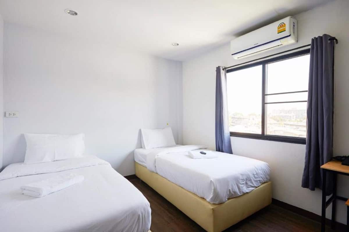 Habitación de hotel con dos camas, una ventana con cortinas, un equipo de aire acondicionado y una mesita.