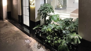 A modern building with a large glass entrance, a potted plant, and a wall-mounted light fixture. - Mia Apartments by XÔI Residences (Hanoi)