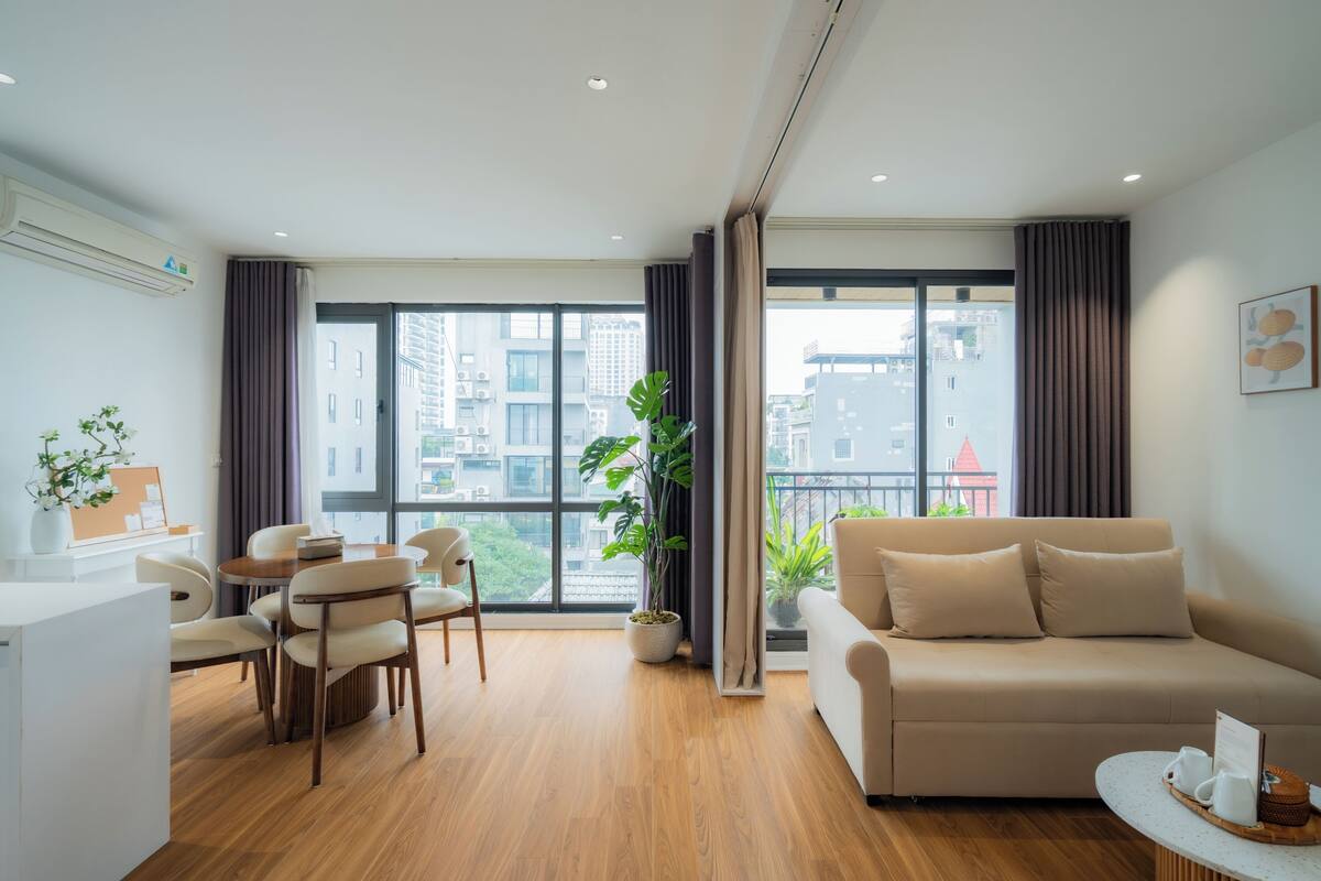 Un salon moderne comprenant un canapé, des fauteuils, une table à manger et une grande fenêtre avec des rideaux.