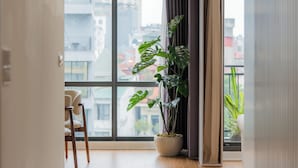 A hallway with a large window, a potted plant, and a chair. - Mia Apartments by XÔI Residences (Hanoi)
