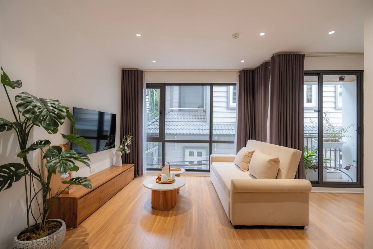 Un salon moderne avec un canapé, un téléviseur, une table basse et de grandes fenêtres avec des rideaux.
