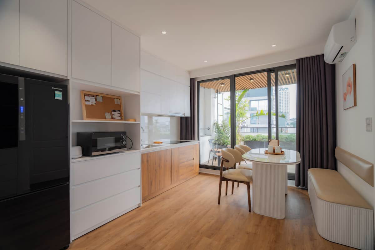 Une cuisine moderne avec des meubles blancs, un réfrigérateur noir, un four à micro-ondes et une table à manger en bois avec des chaises.