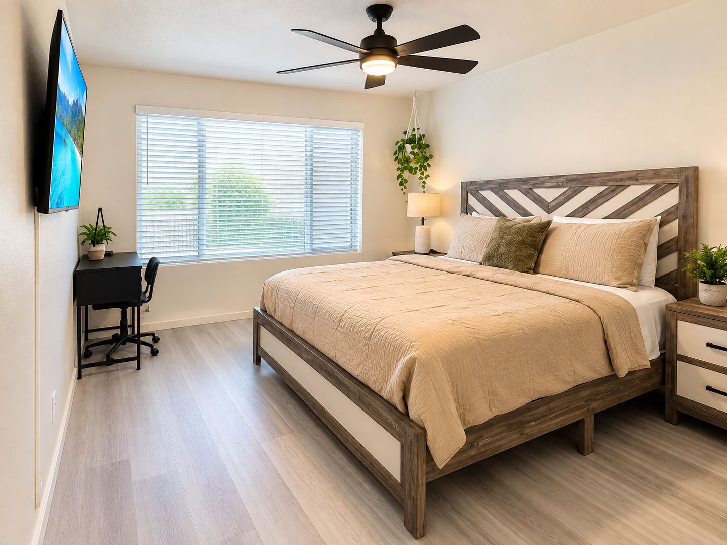 A bedroom with a bed, a desk, a chair, a ceiling fan, a window with blinds, and a wall-mounted TV.
