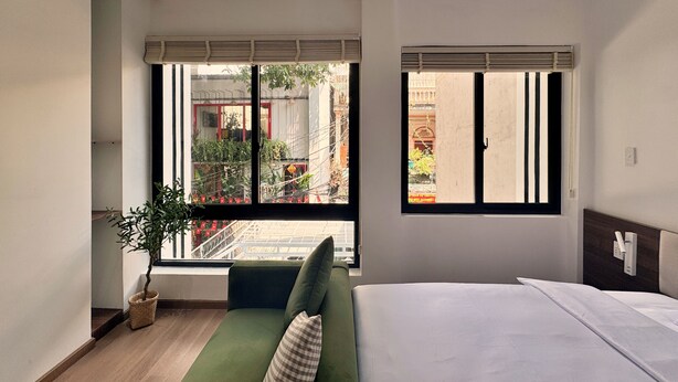 A modern bedroom with a large bed, a window with blinds, a green sofa, and a potted plant. - Miracle Boutique - Near Tan Dinh Church (Ho Chi Minh City)