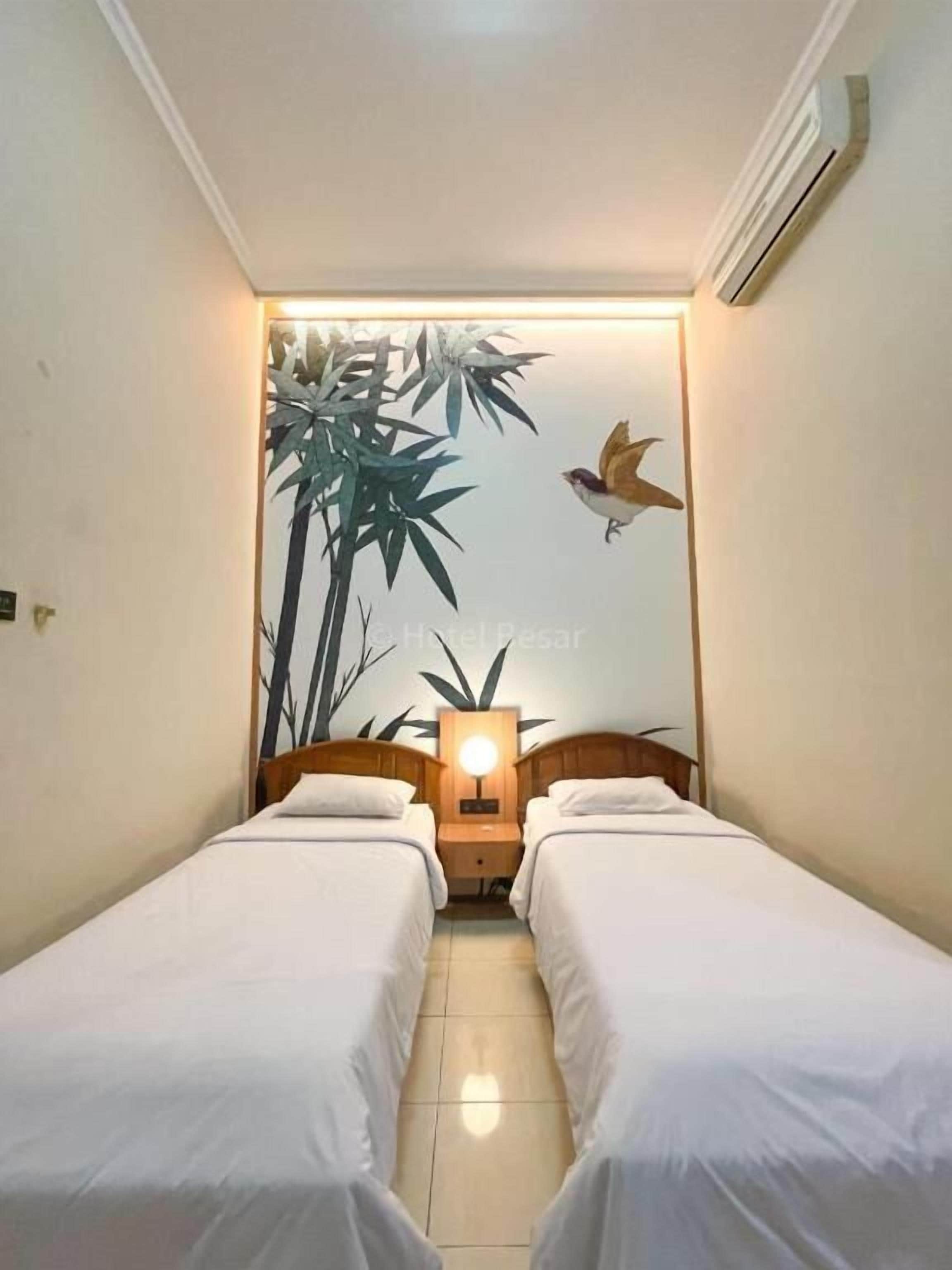 Ein kleines Hotelzimmer mit zwei Einzelbetten, einem Nachttisch mit Lampe sowie einer Wandmalerei mit Bambus und einem Vogel.