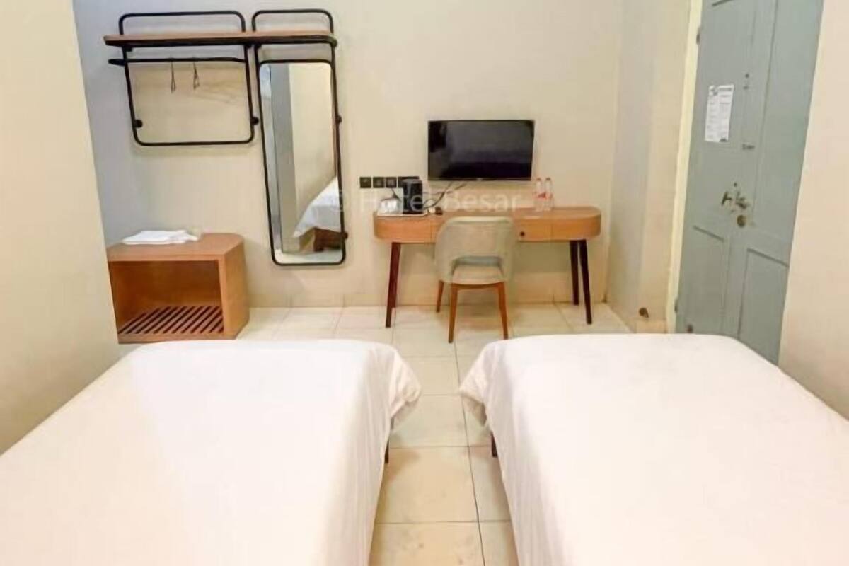 A hotel room with two beds, a desk with a chair, a television, and a wardrobe.