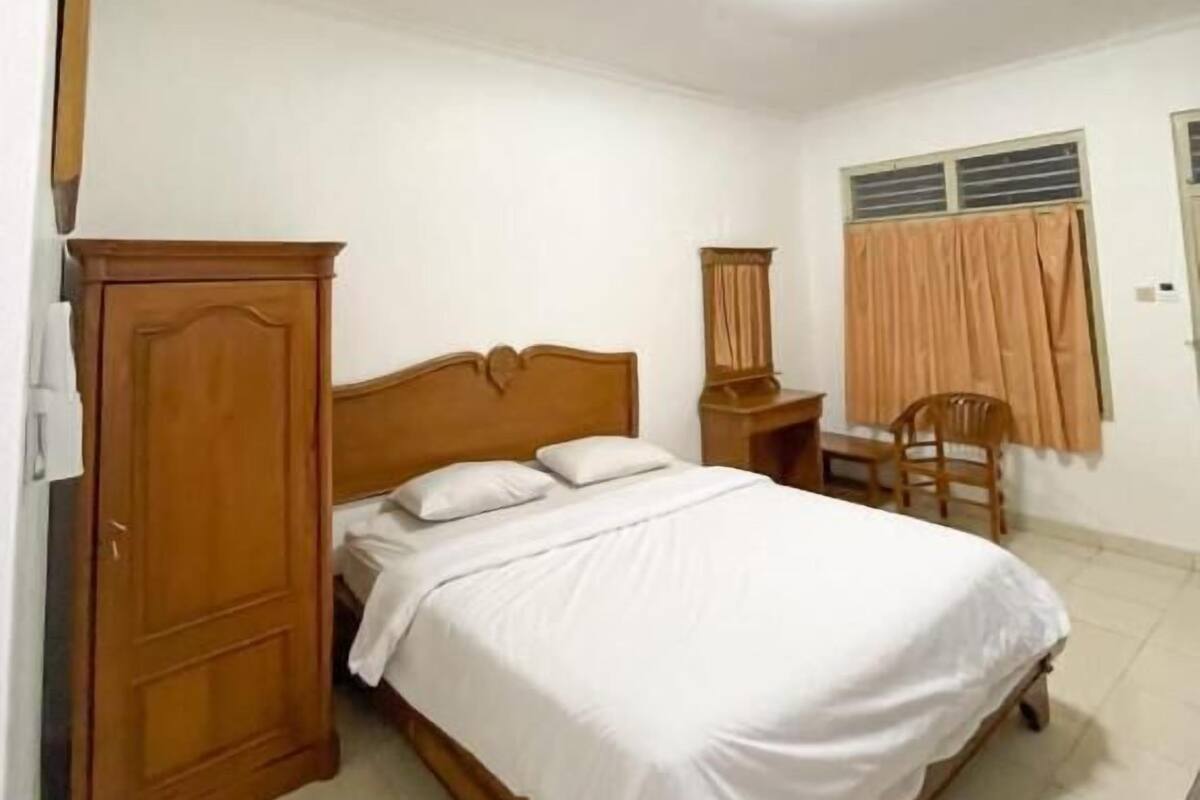 A bedroom with a wooden bed, a nightstand, a wardrobe, a chair, and a window with curtains.