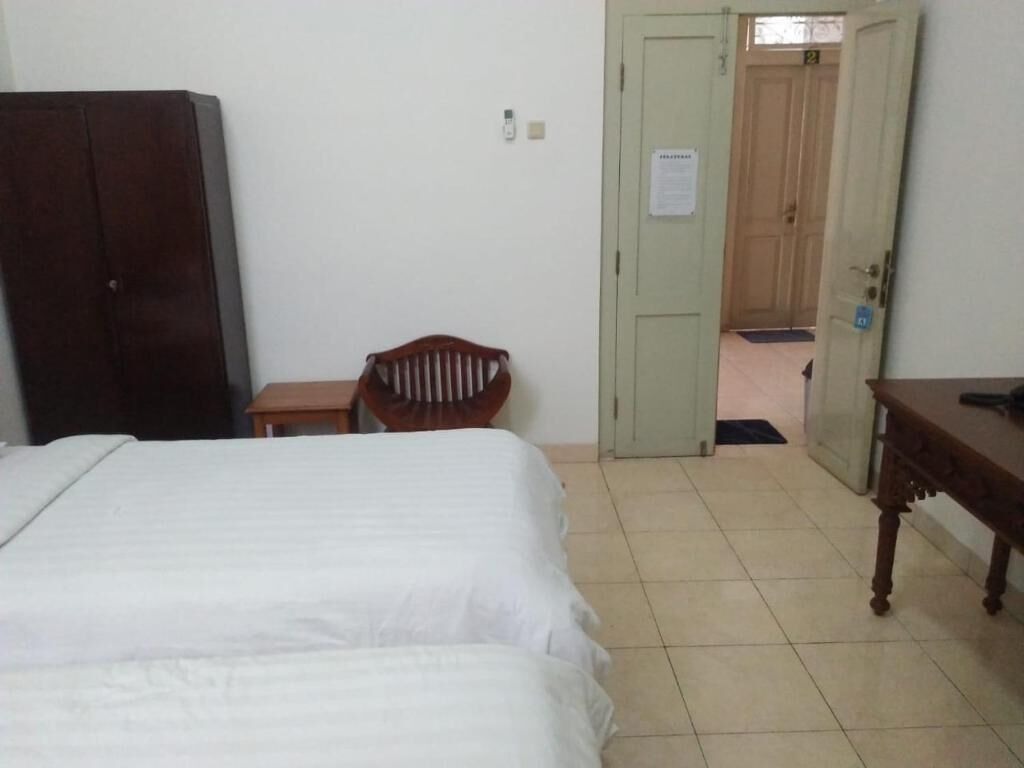 A hotel room with a bed, a wooden chair, a desk, and a wardrobe.