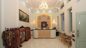 Un hall d’hôtel comprenant un comptoir d’accueil, un lustre, une horloge murale et un porte-vêtements.