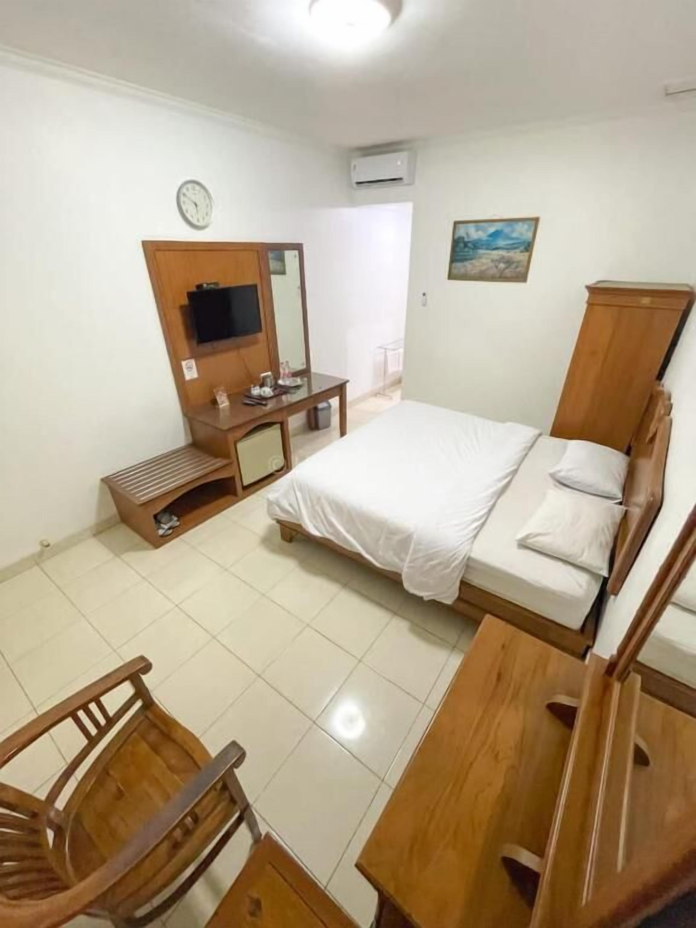 Habitación de hotel con cama, escritorio, silla, televisor, reloj y equipo de aire acondicionado.