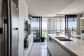 A modern kitchen with a large window, stainless steel appliances, and a view of a cityscape. - Peppers Retreat Atop The Broadbeach Skyline (Gold Coast)