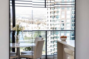 Ein Essbereich mit Tisch, Stühlen, einer Vase mit Blumen und einer Obstschale auf einem Balkon mit Blick auf die Stadt.