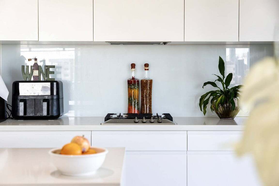 A modern kitchen with a gas stove, two bottles of liquor, a coffee machine, and a bowl of fruit on the counter.