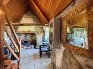 A rustic interior with a stone fireplace, wooden beams, and a dining area with chairs.