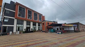 A multi-story building with large windows, a paved entrance area, and a small shop with a sign. - BALAJI HOTEL AND RESTAURANT (Uluberiya)