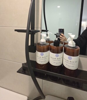 A bathroom with a mirror reflecting three bottles of baby powder, a black hairdryer, and a person taking a photo. - Belin Stay Myeongdong & Jongno (Seoul)