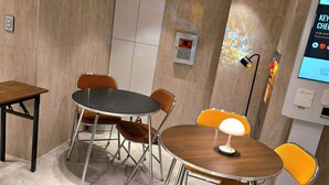 A conference room with a round table, four chairs, a lamp, a fire alarm, and a digital screen displaying a menu. - Belin Stay Myeongdong & Jongno (Seoul)