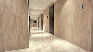 A corridor with marble flooring, recessed ceiling lights, and doors with a red emergency exit sign. - Belin Stay Myeongdong & Jongno (Seoul)