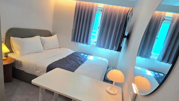 A hotel room with a bed, bedside table, lamp, desk, chair, and a large mirror. - Belin Stay Myeongdong & Jongno (Seoul)