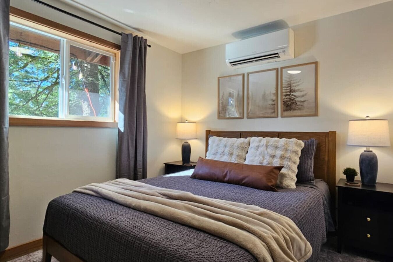 A bedroom with a bed, a window, an air conditioner, and framed pictures on the wall.