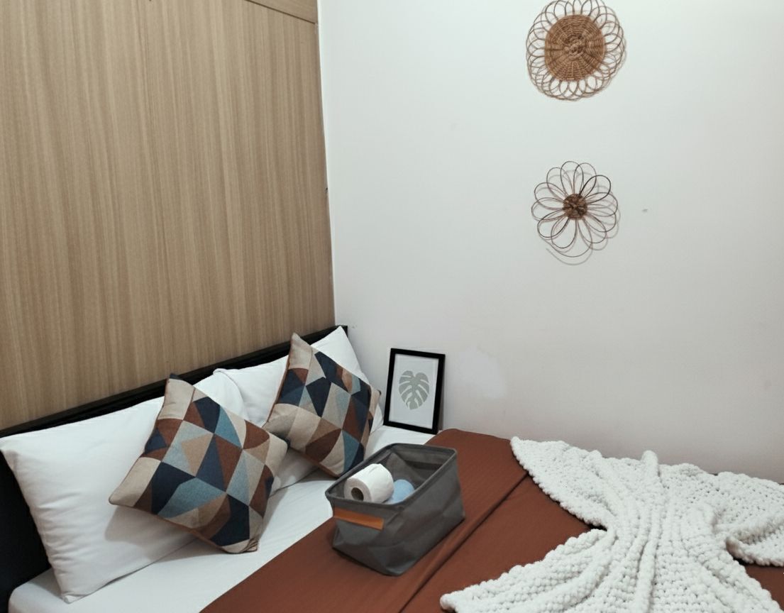 A bed with patterned pillows, a framed picture, a storage box, and a white knitted blanket.