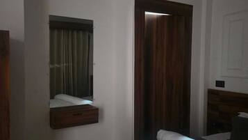 Una habitación de hotel con cama, cabecero de madera, mesita de noche, espejo y puerta.