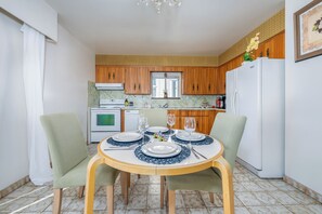 Ein Essbereich mit einem runden Tisch, gedeckt für vier Personen, Holzschränken, einem weißen Kühlschrank und einer Küche im Hintergrund.