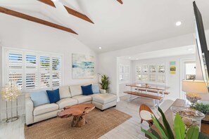 A spacious living room with a sectional sofa, wooden coffee table, and a dining area with benches.