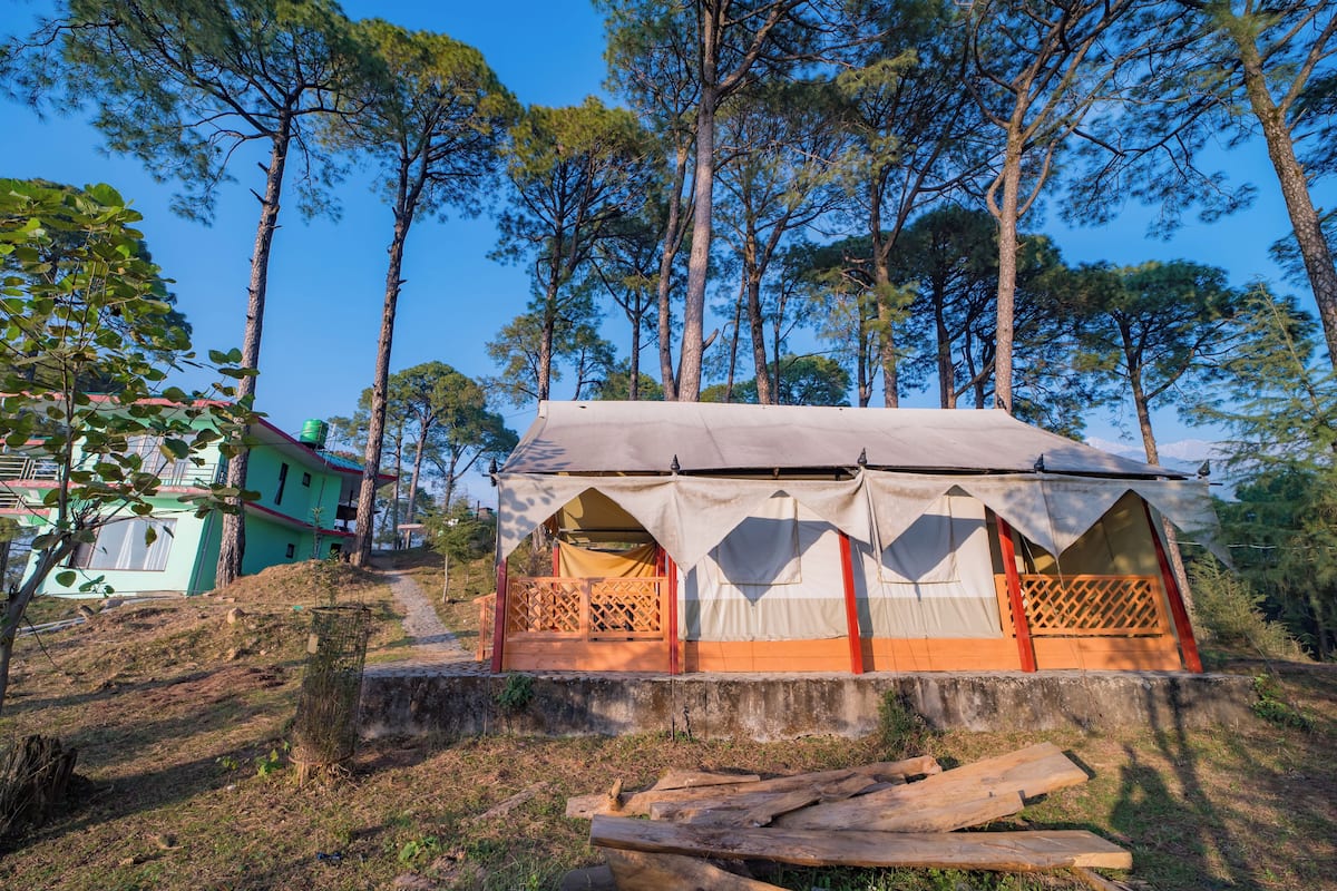 A tented accommodation with a balcony, surrounded by trees and a hillside.