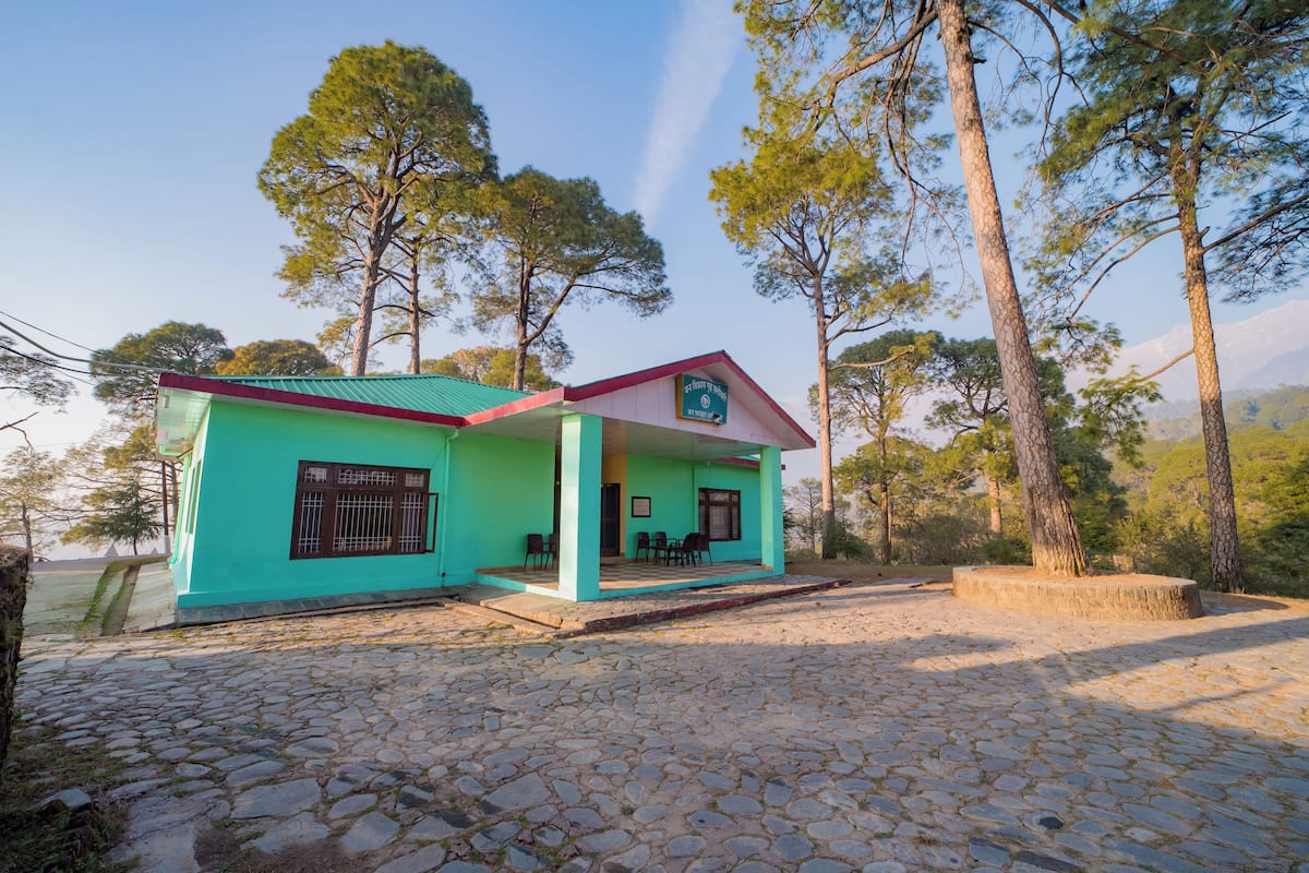 A turquoise building with a red roof, a covered porch, and a stone-paved area.