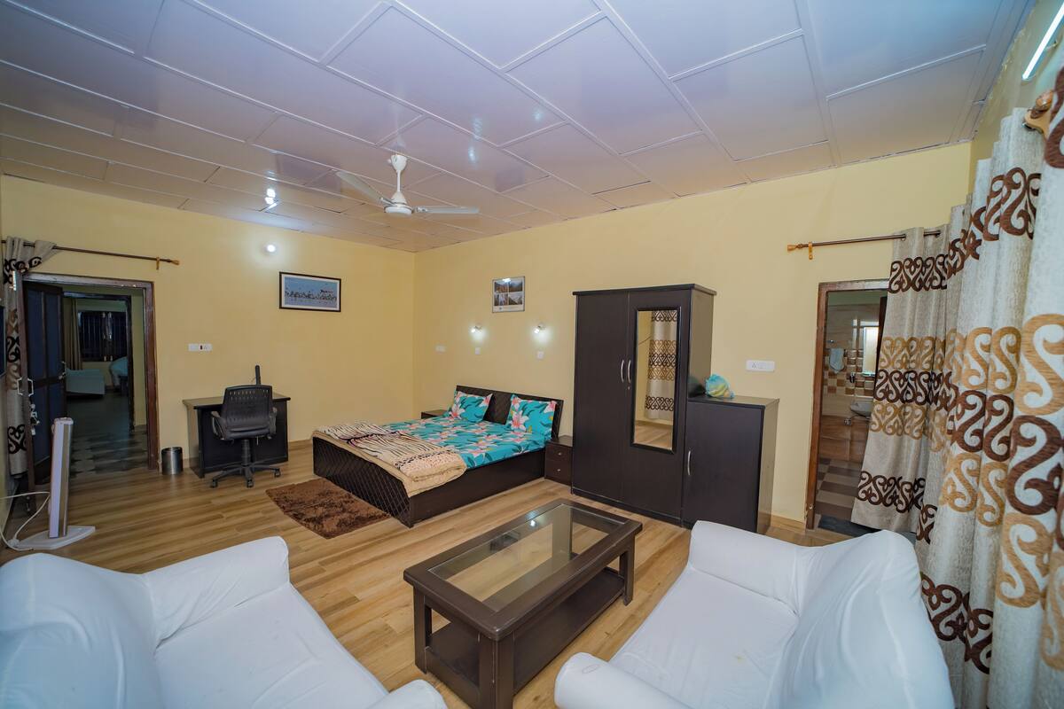 A room with a bed, a desk, a wardrobe, a glass-top coffee table, and a ceiling fan.